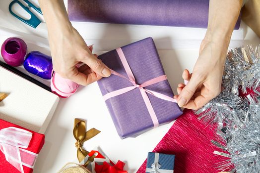 Woman wrapping christmas presents to violet packing paper. woman hands packing a christmas gift, diy gift packing and wrapping concept.