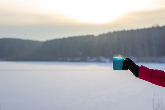 A young woman in a red jacket in winter holds a glass of hot coffee or tea. A snowy winter and a hot drink to keep you warm. Cup of hot coffee or tea