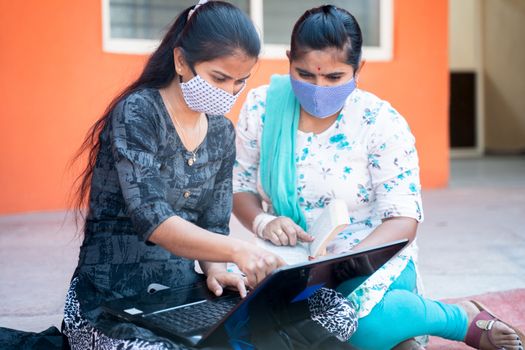 Two young girl college students in medical mask working or studying project on laptop at college - concept of college reopen, new normal due to coronavirus or covid-19 pandemic