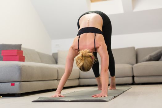 Beautiful blonde woman doing home workout indoors. Woman practice yoga at home. Fit girl using workout tutorials for healthy active lifestyle. Woman using quarantine for home workouts. Stretching