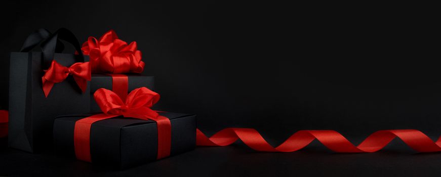 Gift box wrapped in black paper with red ribbon on black background, design banner black friday sale concept copy space for text