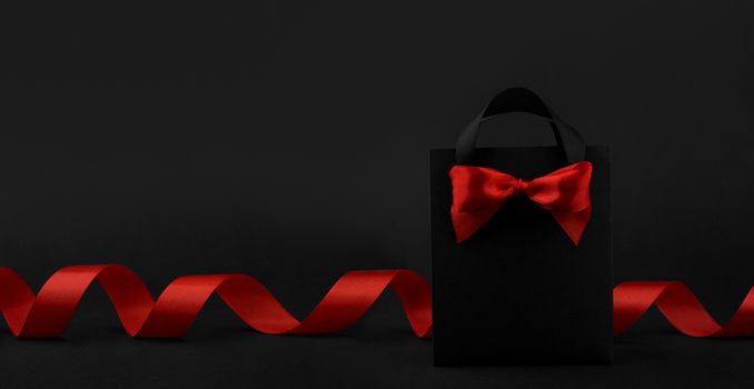 Gift in black paper bag with red ribbon on black background, design banner black friday sale concept copy space for text