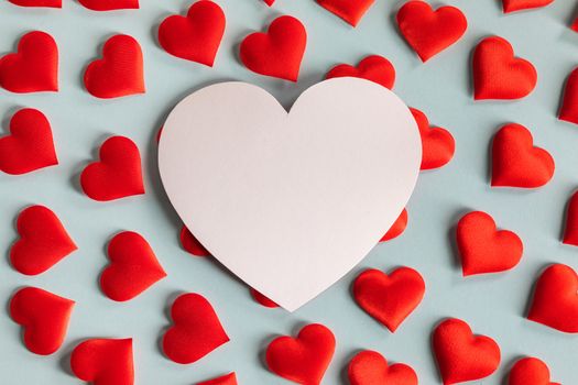 Valentine's day many red silk hearts and white heart shaped card on blue background, love concept