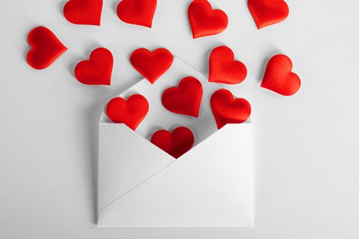 Valentine day love letter, envelope of craft paper with red hearts heap spread on white background.