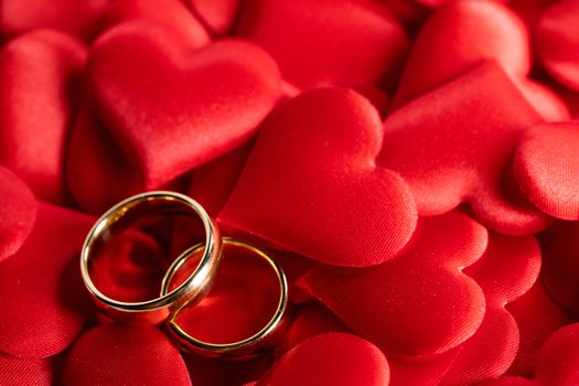 Two golden wedding rings on red hearts background