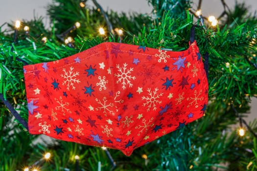 Festive coronavirus face protection design with stars used as seasonal ornament at the branches of an artificial tree.