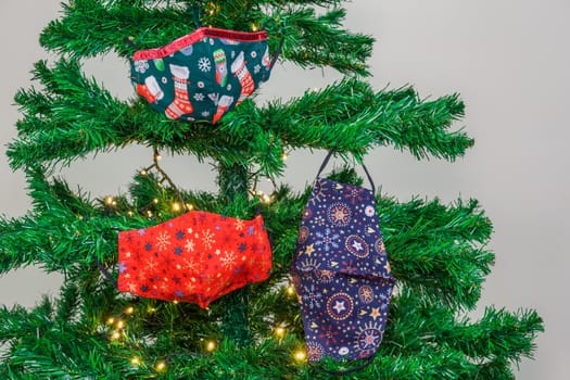 Festive coronavirus face protection designs used as seasonal ornaments at the branches of an artificial tree.