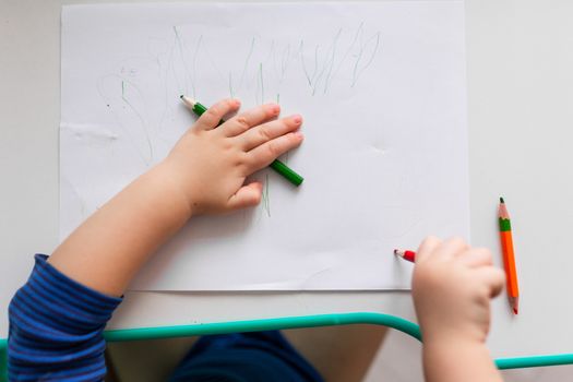 Baby boy drawing a picture with colored pencils, focus on hands
