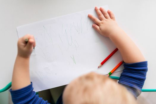 Left handed baby boy drawing a picture with colored pencils