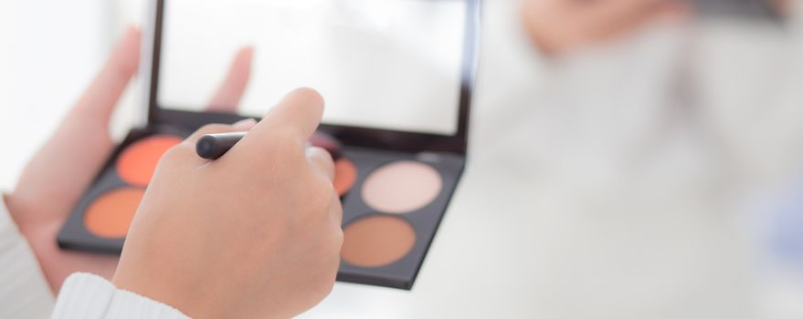 Beauty closeup young asian woman with back view applying makeup with brush cheek on hand, beautiful girl holding blusher rear view, skin care and cosmetic table fashion concept.