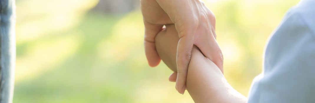 Closeup mother or parent and son holding hand with love together in summer outside in the park, mom take care kid holding palm, child have a trust for mother, family concept, banner website.