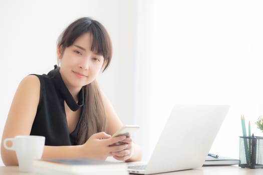 Beautiful young asian woman working laptop computer online to internet and texting message on smart mobile phone, freelance using notebook, business and communication concept.