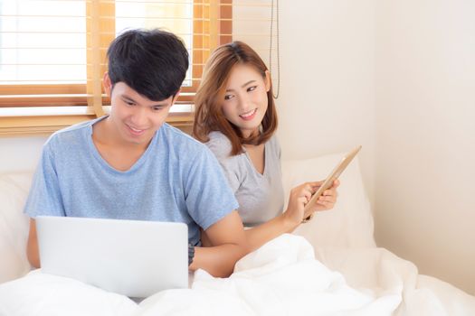 Beautiful young asian couple cheerful freelance working with man using laptop and woman using tablet on couch, family relax and sharing communication together at home, lifestyle concept.