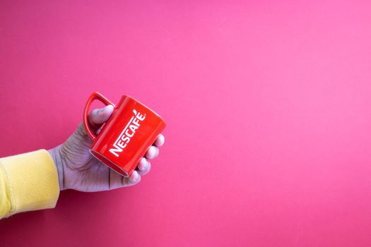Kuala Lumpur, Malaysia - November 12, 2020 : Hand holding Nescafe Mug on red background