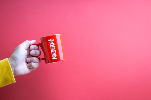 Kuala Lumpur, Malaysia - November 12, 2020 : Hand holding Nescafe Mug on red background