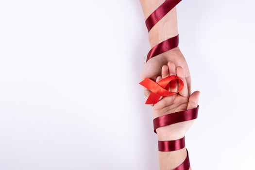 Aids awareness, man and woman hands holding red ribbon on white background with copy space for text. World Aids Day, Healthcare and medical concept.