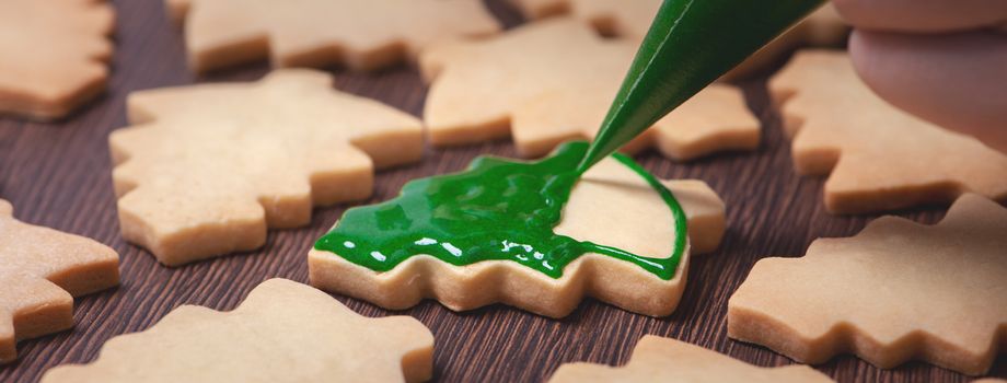 Close up of drawing gingerbread Christmas tree sugar cookie on wooden table background with green icing, concept of holiday celebration.