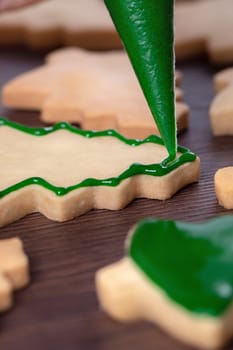 Close up of drawing gingerbread Christmas tree sugar cookie on wooden table background with green icing, concept of holiday celebration.