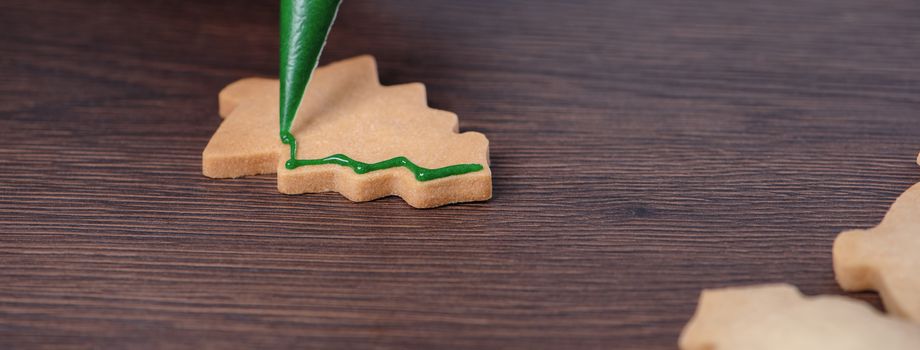 Close up of drawing gingerbread Christmas tree sugar cookie on wooden table background with green icing, concept of holiday celebration.