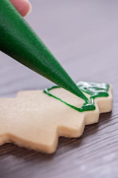 Close up of drawing gingerbread Christmas tree sugar cookie on wooden table background with green icing, concept of holiday celebration.