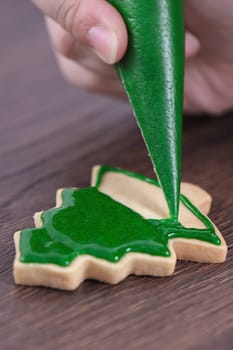Close up of drawing gingerbread Christmas tree sugar cookie on wooden table background with green icing, concept of holiday celebration.