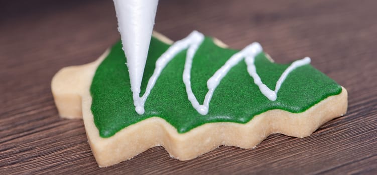 Close up of drawing gingerbread Christmas tree sugar cookie on wooden table background with green icing, concept of holiday celebration.