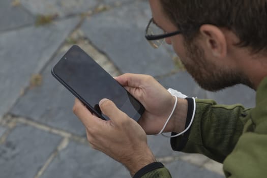 A young man, grabbing a protective face mask, holds a smart mobile phone, Spain.