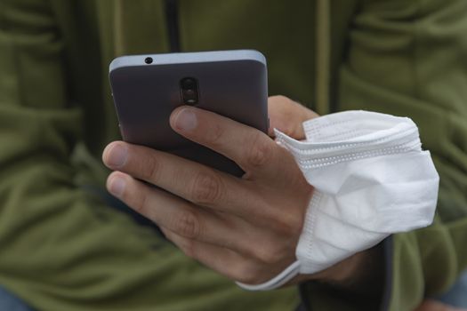 A young man, grabbing a protective face mask, holds a smart mobile phone with his hand, Spain.