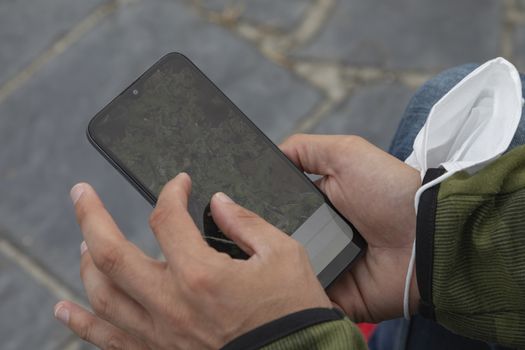 A young man, grabbing a protective face mask, search something with a smart mobile phone, Spain.