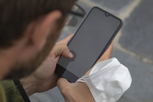 A young man, grabbing a protective face mask, holds a smart mobile phone, Spain.