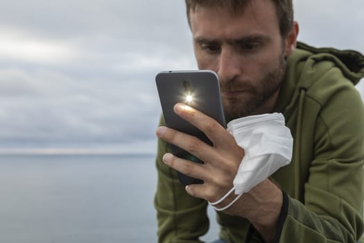 A young man, with a protective face mask, takes a photograph with a smart mobile phone, Spain.