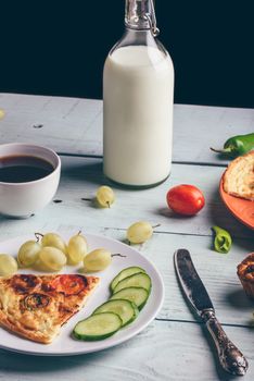 Frittata and fruits, vegetables, bottle of milk, cup of coffee over light wooden background. Healthy breakfast concept.