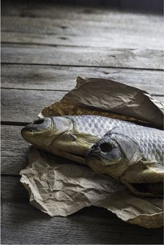 Salted Dry fish vobla on crumpled craft paper on wooden background, delicious beer snack, close-up.