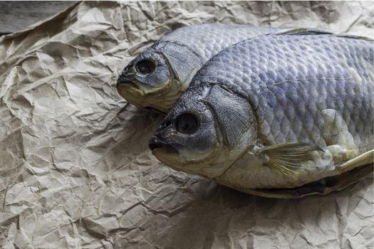 Salted Dry fish vobla on crumpled craft paper on wooden background, delicious beer snack, close-up.