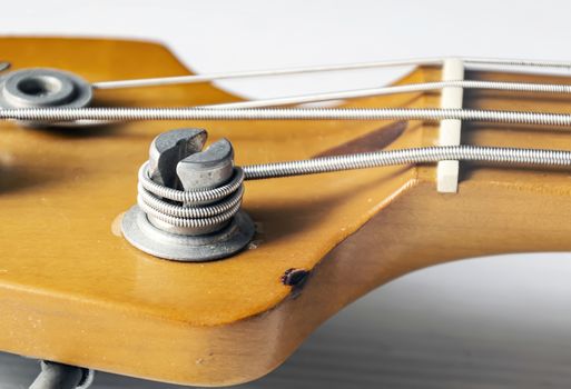 Detail of a tuning post on the wooden headstock of an electric bass guitar. Musical instruments and mechanics for string tuning.