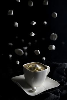 Cup of coffee and marshmallows on black background.