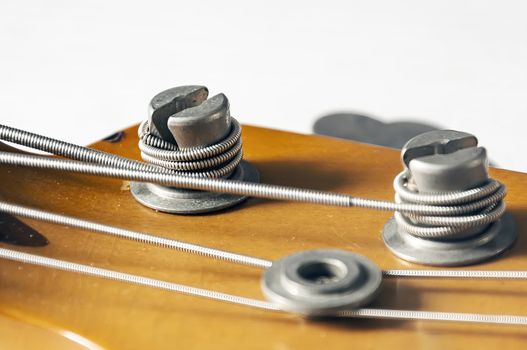 Detail of a tuning post on the wooden headstock of an electric bass guitar. Musical instruments and mechanics for string tuning.