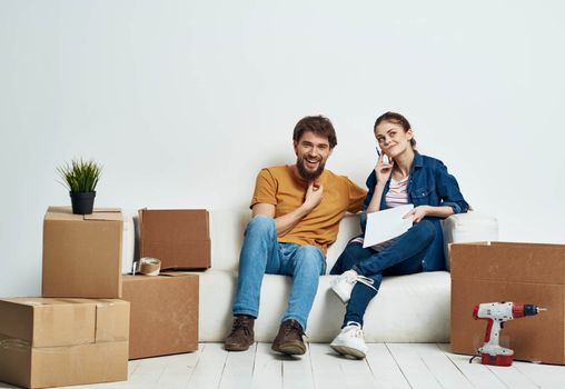 man and woman sitting on a white sofa in a room with boxes of things tools moving. High quality photo
