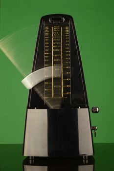 A vertical composition of a working musical metronome over a green background.