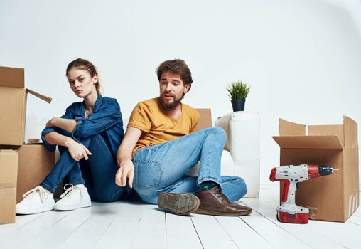 A man and a woman are sitting on the floor indoors near the couch and moving boxes. High quality photo