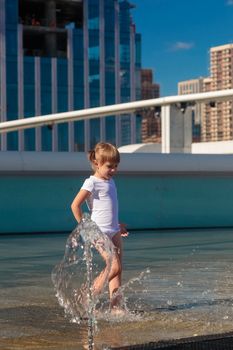 A little girl splashes water from a fountain on the territory of the Moscow city business center