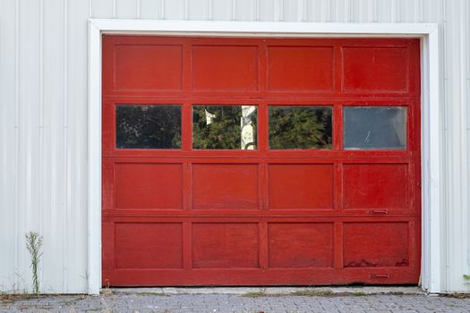 A wooden garage door painted red with glass windows and metal handles is surrounded by a white wall.