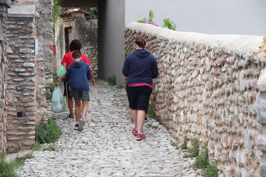 people walking between historic walls, seen from behind