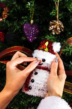 Hands holding Christmas snowman figurine in front of the Christmas tree. Decorating the fir tree isolated