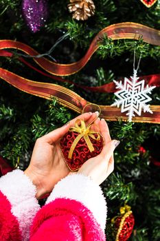 Hands holding Christmas ornament in front of Christmas tree. Decorating fir branches with Christmas decorations.