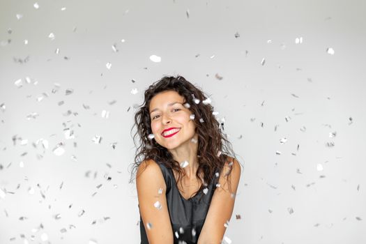 The emotion of success. Happy sexy brunette girl is enjoying celebrating with confetti on a white background.