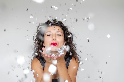 The emotion of success. Happy sexy brunette girl is enjoying celebrating with confetti on a white background.