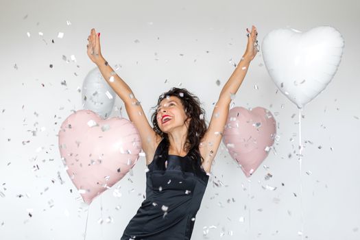 The emotion of success. Happy sexy brunette girl enjoying celebrating with confetti and heart balloons on a white background.