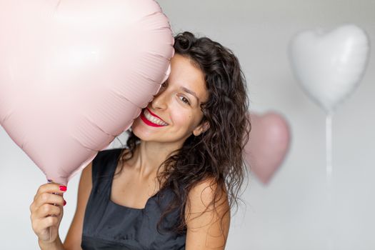 Sexy brunette girl posing with heart-shaped balloons on a white background.