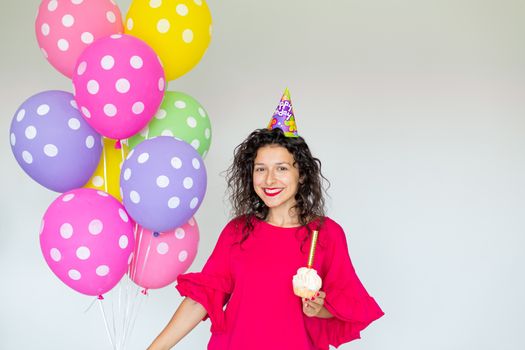 Happy Birthday. Sexy brunette girl posing with balloons, fireworks, colorful balloons and holiday cake on a white background.